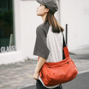 Detail of a bright orange nylon messenger bag shown in a stylish outdoor streetwear setting