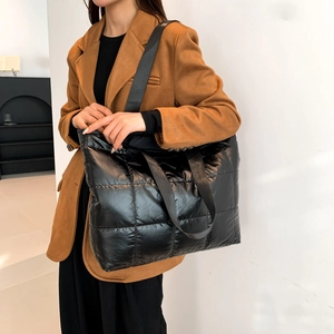 Close-up of black quilted tote bag texture showing glossy nylon finish and shoulder strap