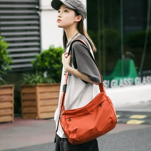 Detail of a large orange nylon crossbody bag with side pockets and adjustable strap