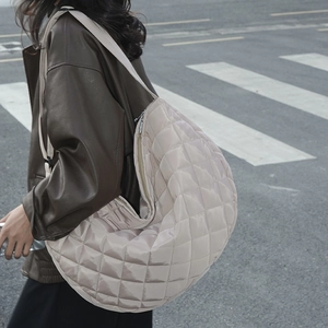 Vue de rue d'un sac demi-lune en nylon beige matelassé porté sur une veste en cuir brun