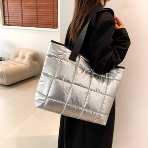 Detail view of metallic silver quilted puffer tote bag with black woven straps shown on model