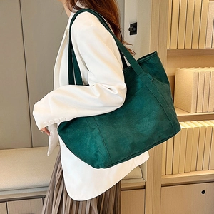 Close-up of a large dark green suede tote bag with wide shoulder strap on a model