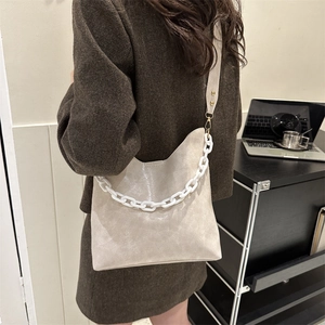 Detail of beige shoulder bag with decorative chunky white chain and gold-tone hardware