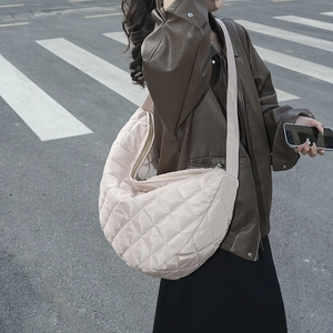 Sac bandoulière en nylon matelassé beige porté par un mannequin dans un décor de rue