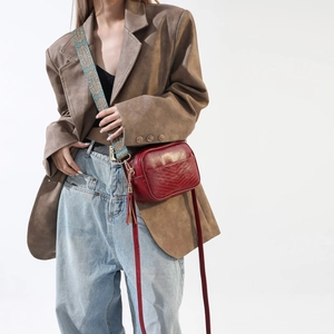 Detail of burgundy crossbody bag with V-shaped quilting and wide woven shoulder strap