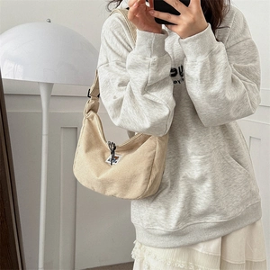Model wearing a beige corduroy half-moon crossbody bag with a bear logo patch detail