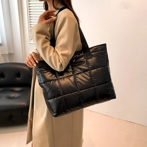 Close-up of black quilted puffer tote bag with wide strap worn on a beige trench coat