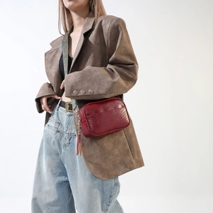 Detail of burgundy PU crossbody bag featuring V-shaped stitching and tassel accent