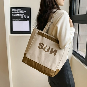 Detail shot of beige canvas tote bag with SUN logo pattern worn over the shoulder