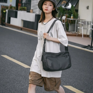 Outdoor street shot of a large black nylon crossbody bag with dual zipper pockets