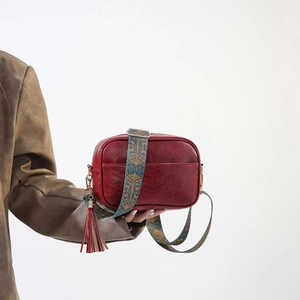Detail of red PU leather bag with V-shaped stitching and ethnic embroidered strap