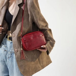 Detail of burgundy PU crossbody bag with V-quilted texture and gold tassel charm