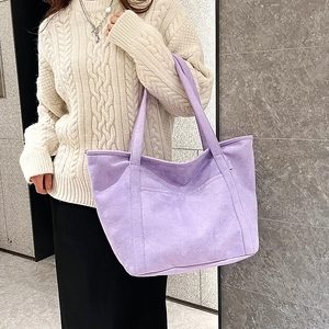 Close-up of a large purple faux suede tote bag worn with a casual beige sweater