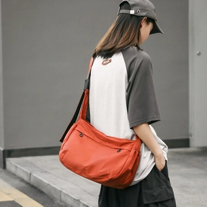 Detail view of a large orange nylon crossbody bag with adjustable wide black strap