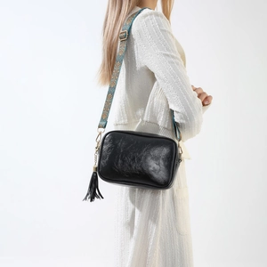Détail d'un sac caméra en PU noir brillant avec bandoulière ethnique et gland en cuir