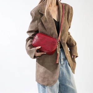Detail of burgundy PU leather crossbody bag with V-shaped stitching and tassel accent