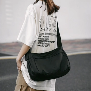 Detail of a large black waterproof nylon messenger bag worn by a model in a casual setting