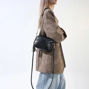 Detail of minimalist black PU leather underarm bag with decorative tassel on brown blazer