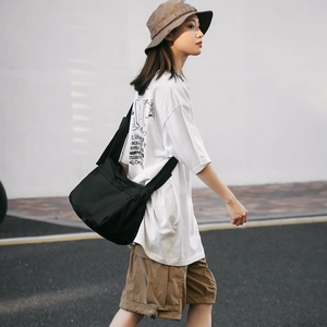Street style shot of a black nylon messenger bag paired with a white printed tee