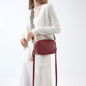 Détail du sac caméra en cuir PU bordeaux avec bandoulière ethnique et pompon décoratif