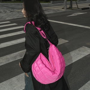 Détail de la texture d'un sac bandoulière en nylon matelassé rose néon avec zip argenté