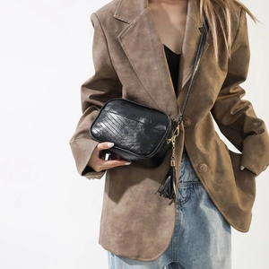 Detail view of black quilted crossbody bag with tassel and gold hardware on a model