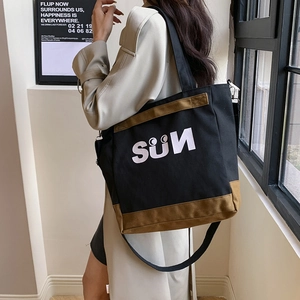 Detail of canvas tote bag with SUN logo and brown leather stitching base on shoulder