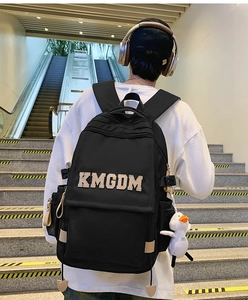 Detail of black nylon backpack featuring white duck charm and KMGDM letter patch