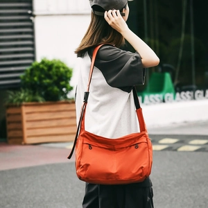 Outdoor model showing vibrant orange nylon crossbody bag with dual front zipper pockets
