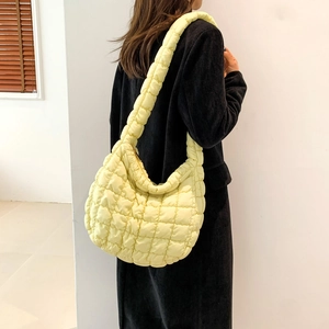 Detail of light yellow quilted puffy shoulder bag with soft square texture on black coat