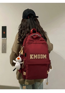 Detail of burgundy nylon backpack featuring KMGDM letter patch and white duck plush charm