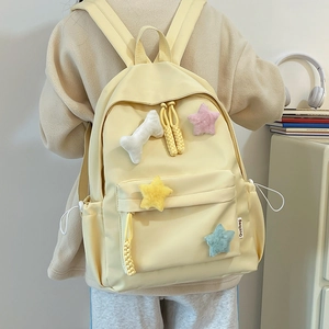 Détail d'un sac à dos en nylon jaune clair avec étoiles en peluche et charme d'os mignon