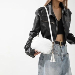 Gros plan d'un sac à bandoulière blanc avec texture litchi et gland en cuir sur le côté