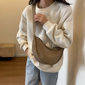Minimalist brown half-moon crossbody bag in nylon fabric worn by model in a cozy room