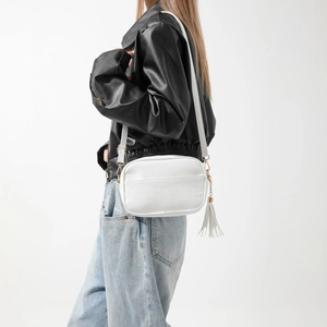 Détail d'un sac bandoulière blanc en cuir grainé avec pompon et finitions dorées chic