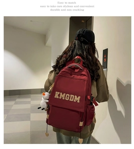 Close-up of wine red nylon backpack with KMGDM embroidery and white duck plush charm