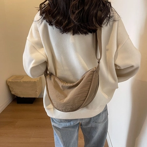 Detail of a dark khaki nylon crescent crossbody bag worn on a model in a minimalist room