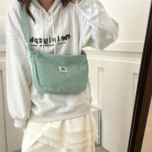 Close-up of light green corduroy crossbody bag with cute bear patch on grey sweatshirt