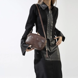 Detail of dark brown leather crossbody bag featuring V-shaped stitching and tassel charm