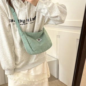 Close-up of light green corduroy crossbody bag featuring a cute bear label detail