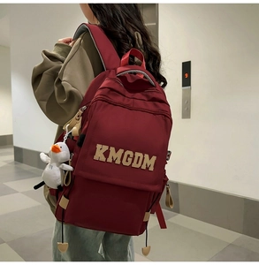 Detail of burgundy nylon backpack featuring white logo embroidery and a cute plush duck charm