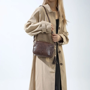 Détail du sac bandoulière carré marron foncé avec pompon à franges et texture vintage