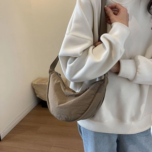 Khaki crescent-shaped nylon crossbody bag worn by a model in a minimalist room
