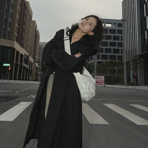 Gros plan sur un grand sac matelassé blanc porté avec un trench-coat noir élégant
