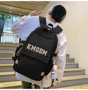 Detail of black nylon backpack with KMGDM embroidery and cute white duck pendant accessory