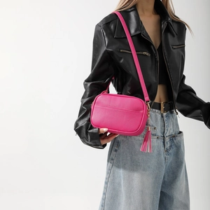 Vue macro du sac caméra rose rouge en cuir grainé avec détail de franges chic