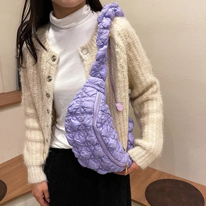 Détail d'un sac demi-lune matelassé violet porté sur un pull en maille beige clair