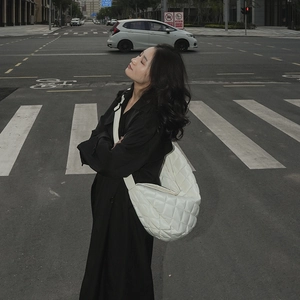 Détail d'un sac demi-lune blanc matelassé avec bandoulière porté par une femme en noir