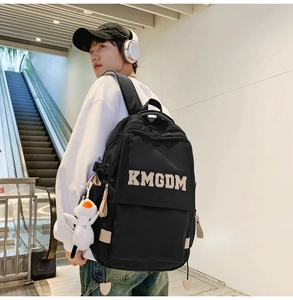Detail of black nylon backpack with white KMGDM embroidery and cute duck plush charm