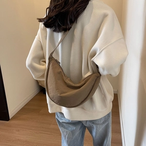 Side view of a dark beige nylon half-moon crossbody bag worn by a model in a minimalist room